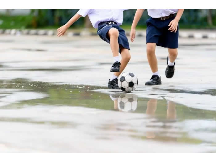 濡れているグラウンドでサッカーをしている少年たち