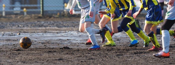 濡れている土の上でサッカーをしている少年たち